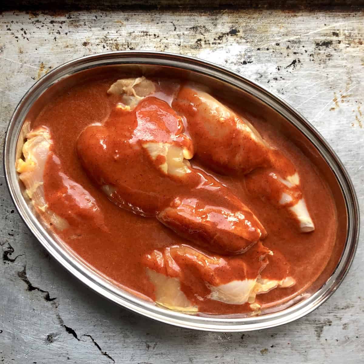 Two large skinless boneless chicken thighs mostly covered with pollo asado marinade ready to marinate.