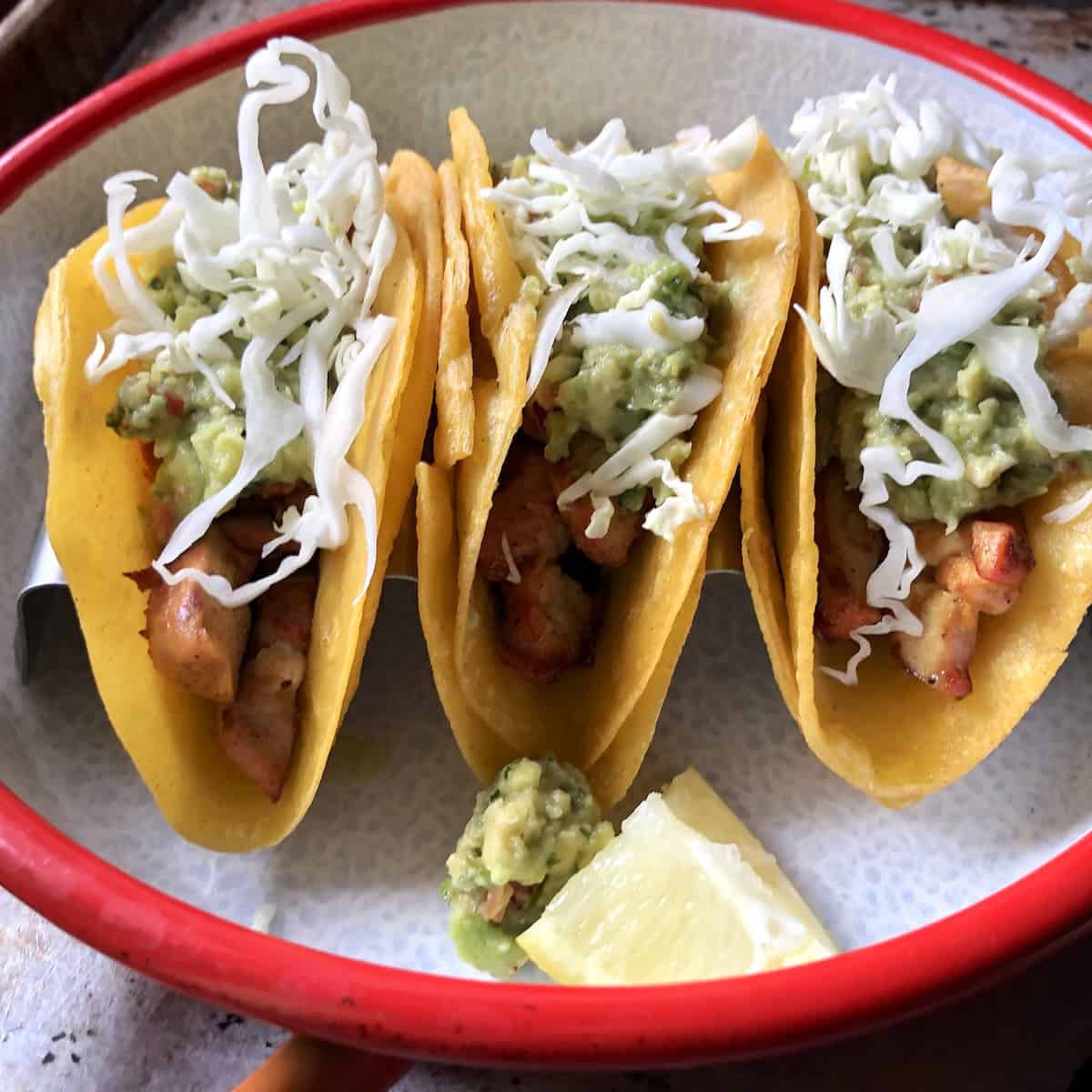 Three pollo asado chicken tacos topped with homemade guacamole and shredded white cabbage in a stainless steel taco holder as I build up the toppings. 
