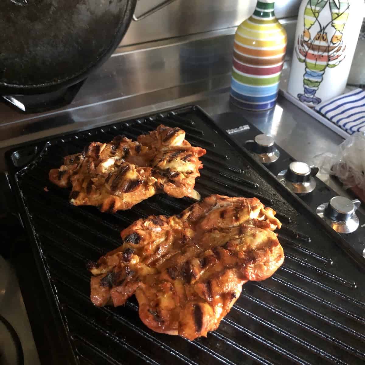 Perfectly grilled pollo asado chicken thighs with grill marks ready to remove to a plate and rest before slicing, showing the perfecct doneness for pollos asados al carbon.

