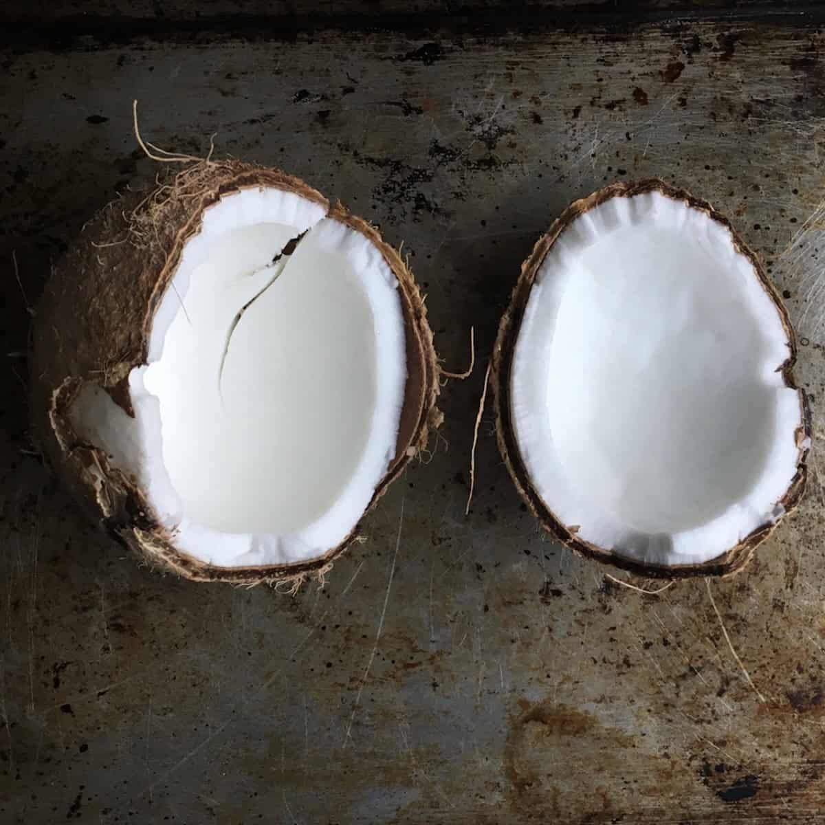 A whole coconut split in half revealing the white flesh.

