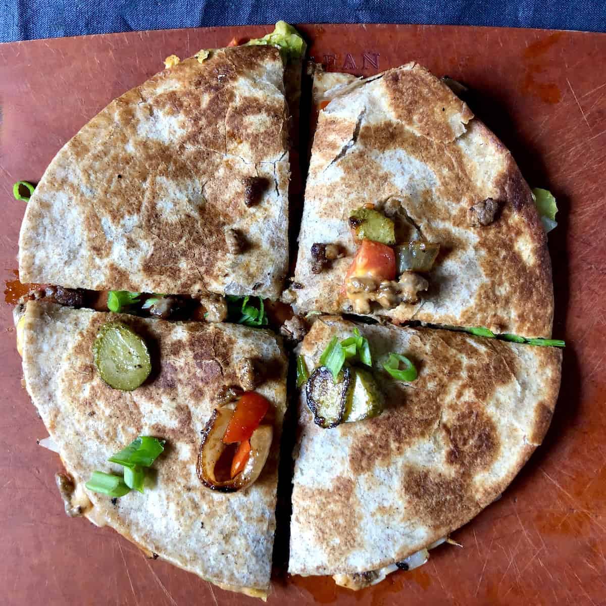 A cheeseburger quesadilla layered using 2 tortillas and cut into four total wedges like a pizza pie showing the alternative way to fold a quesadilla (it's messier). 
