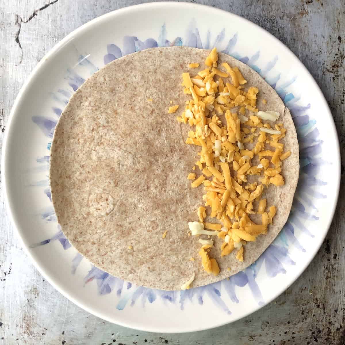 Cheddar and monterey jack cheese spread over half of a whole wheat flour tortilla for a chicken and cheese quesadilla.

