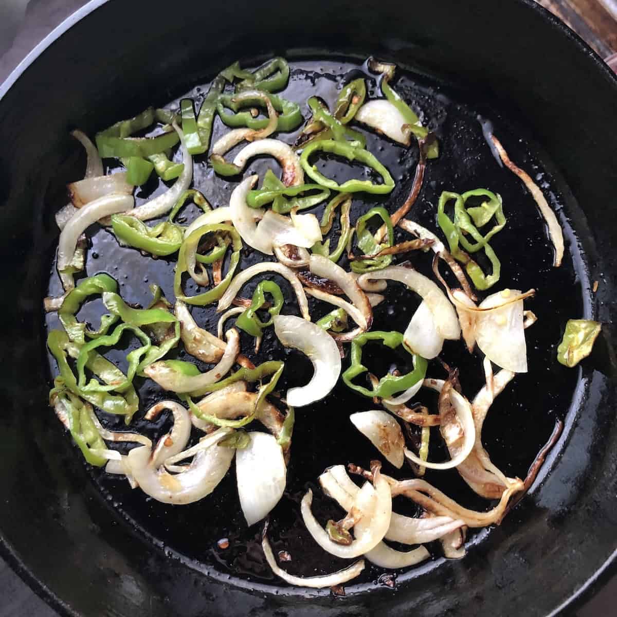 Caramelized onions and cubanelle peppers in a cast iron skillet for a chicken quesadilla recipe.
