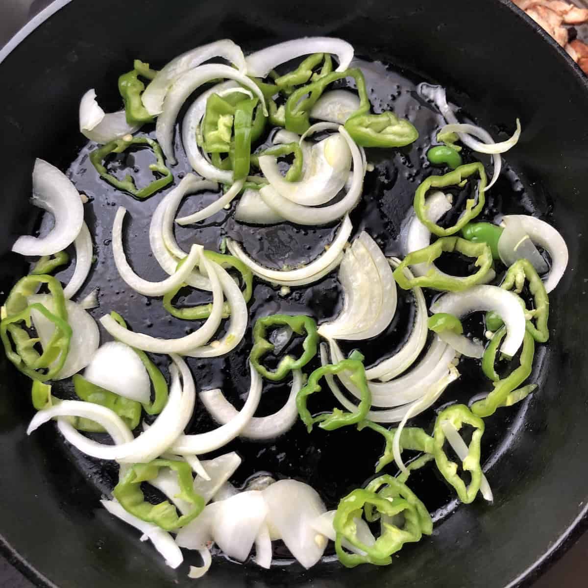 Sliced cubanelle peppers and onions with olive oil in a cast iron skillet ready to caramelize for a chicken quesadillas recipe.
