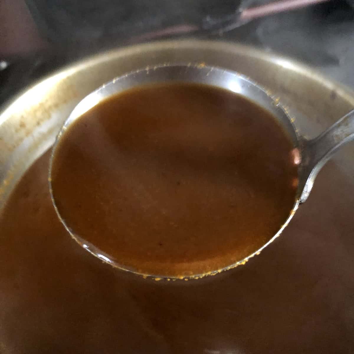 A ladle of perfectly cooked chicken tortilla soup broth ready to fill the garnished bowls.
