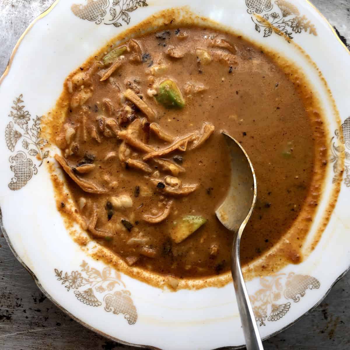 A spoonful of creamy chicken tortilla soup with softened tortilla strips lifted from the bowl showing the rich texture.
