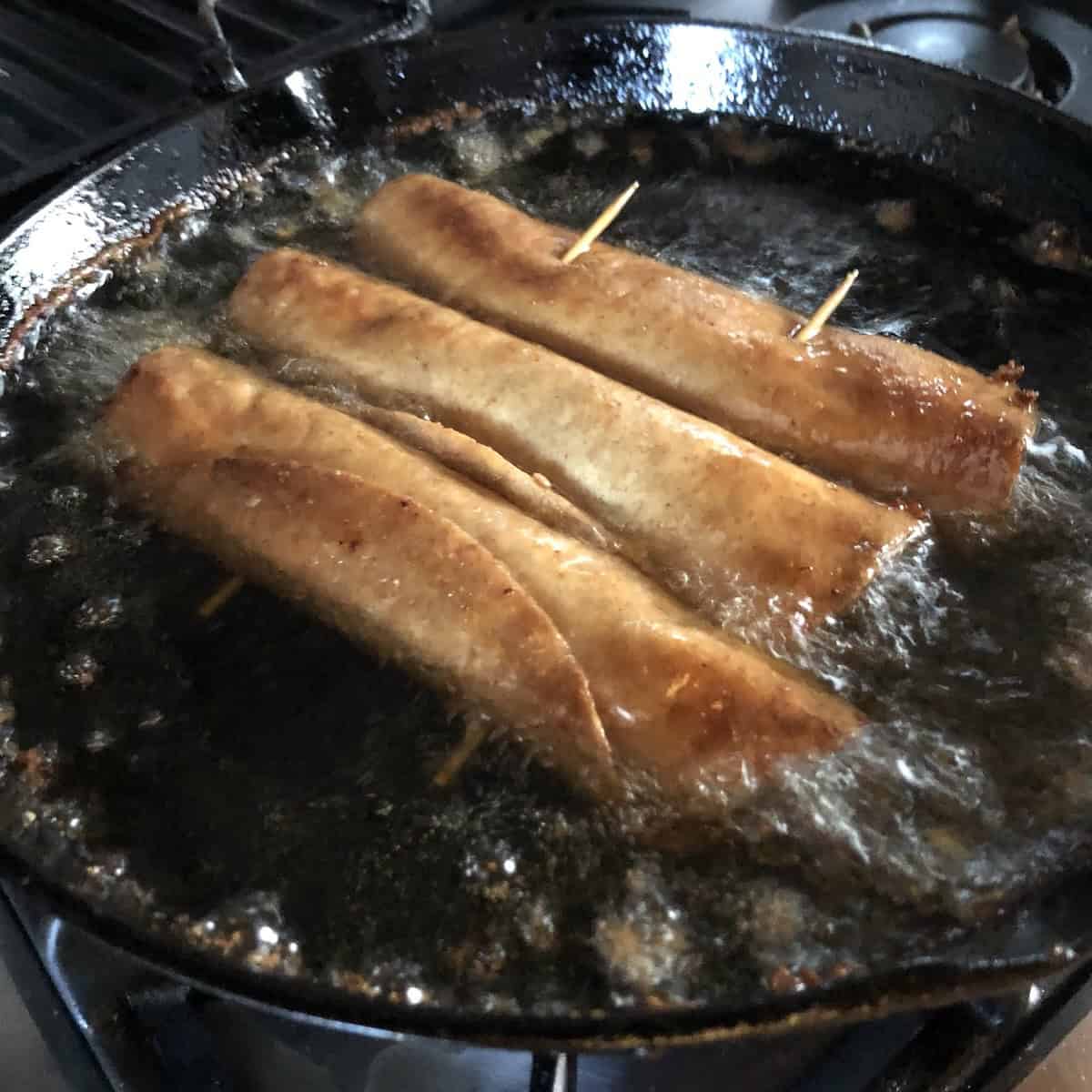 Frying chicken flautas in a cast iron skillet with about 1 inch of oil in it, ready to remove and drain.
