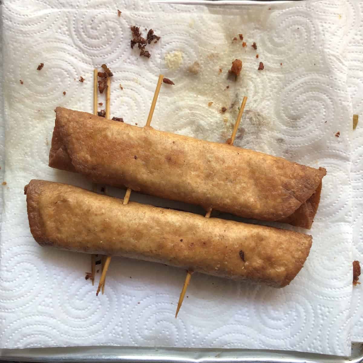 Fried golden brown mexican flautas on a paper towel lined plate ready to remove the skewers.
