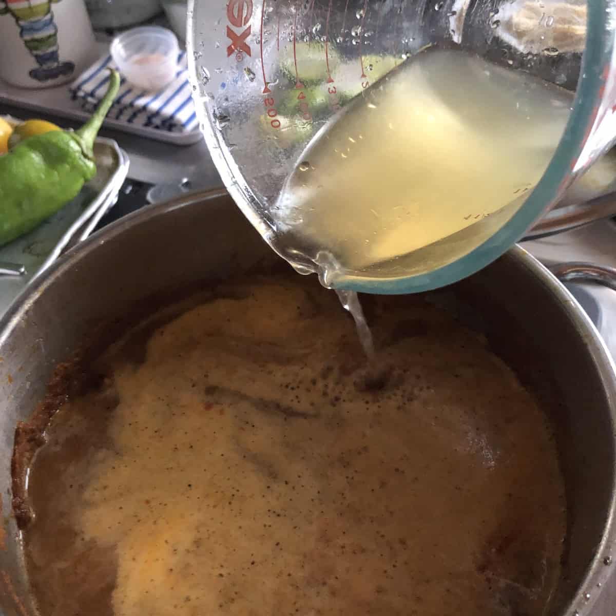 Chicken broth being poured into the reduced chile tomato mixture to cook for 30 minutes.
