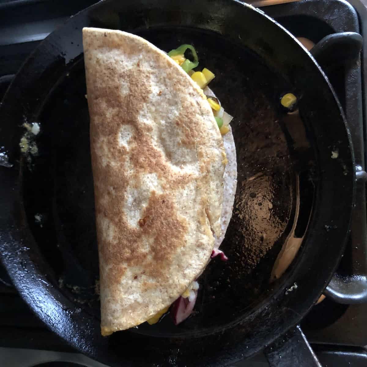 A chicken quesadilla cooking in a well-seasoned cast iron skillet with a little olive oil
