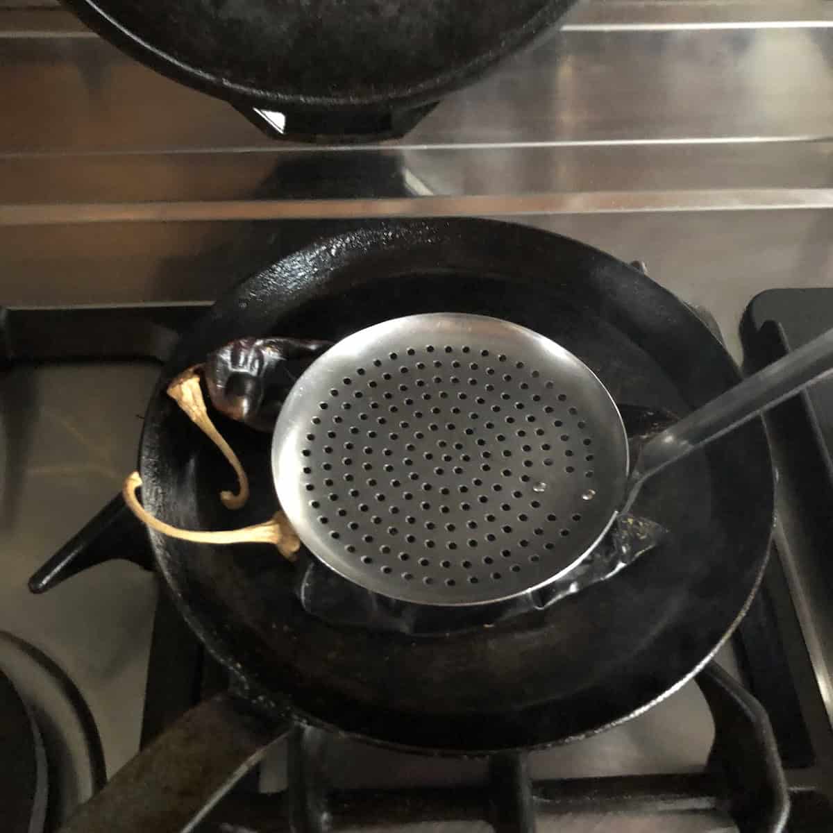 Guajillo chiles being pressed flat with a spatula in a hot dry skillet for how to make tortilla soup from scratch.
