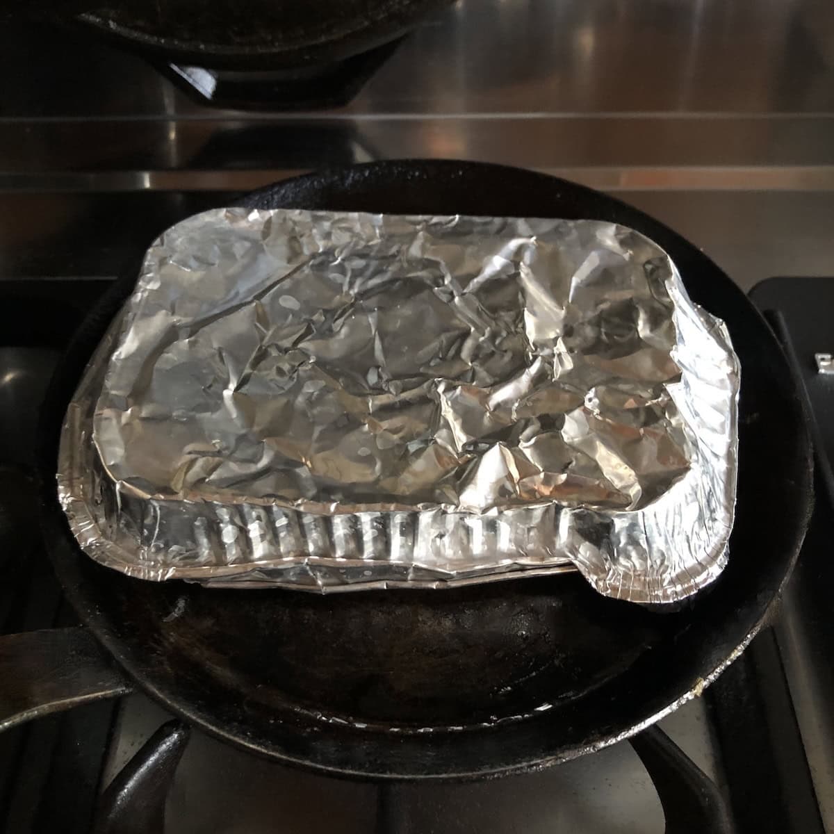 Chicken flautas covered with a disposable aluminum pan to trap steam while reheating in the shallow-edged crepe pan skillet, showing how to reheat flautas for one person instead of using a regular skillet and lid.
