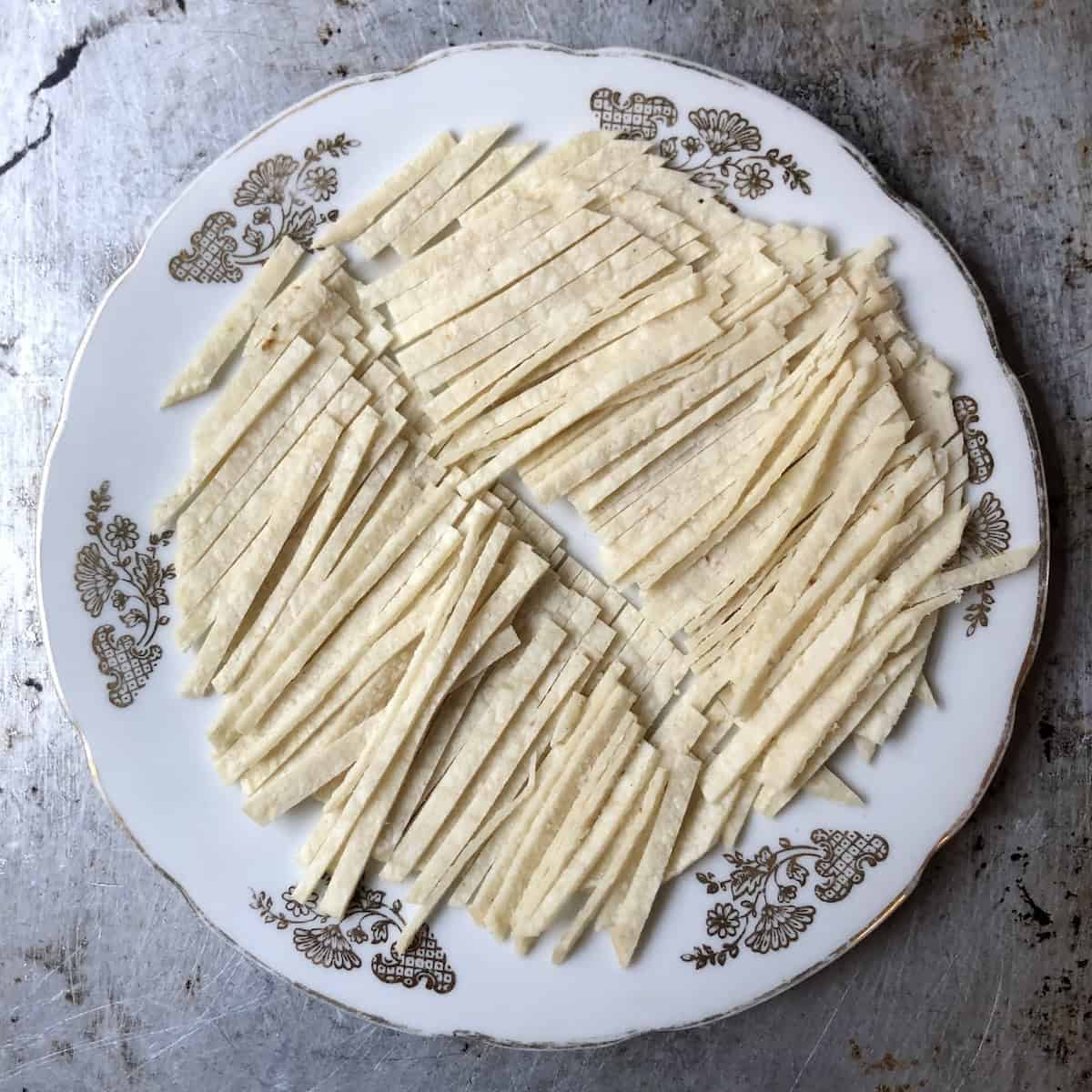 A stack of corn tortillas cut into strips and halved in the middle for shorter pieces that are easier to eat in chicken tortilla soup.
