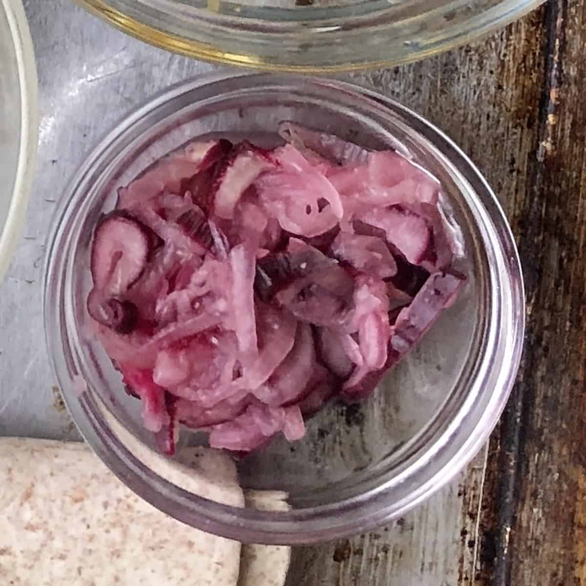 A small bowl of pink colored , thinly sliced, quick pickled shallots ready for adding acidity to mexican recipes like quesadillas, enchiladas, fajitas, flautas, etc.
