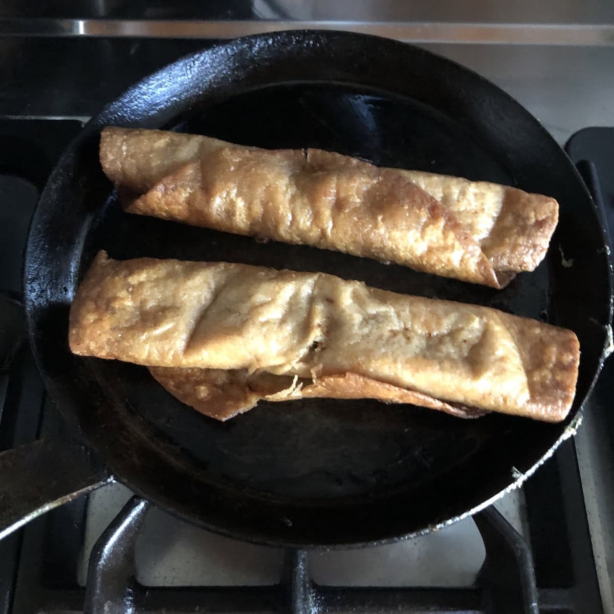 Chicken flautas added to a cast iron crepe pan to reheat and keep crispy.
