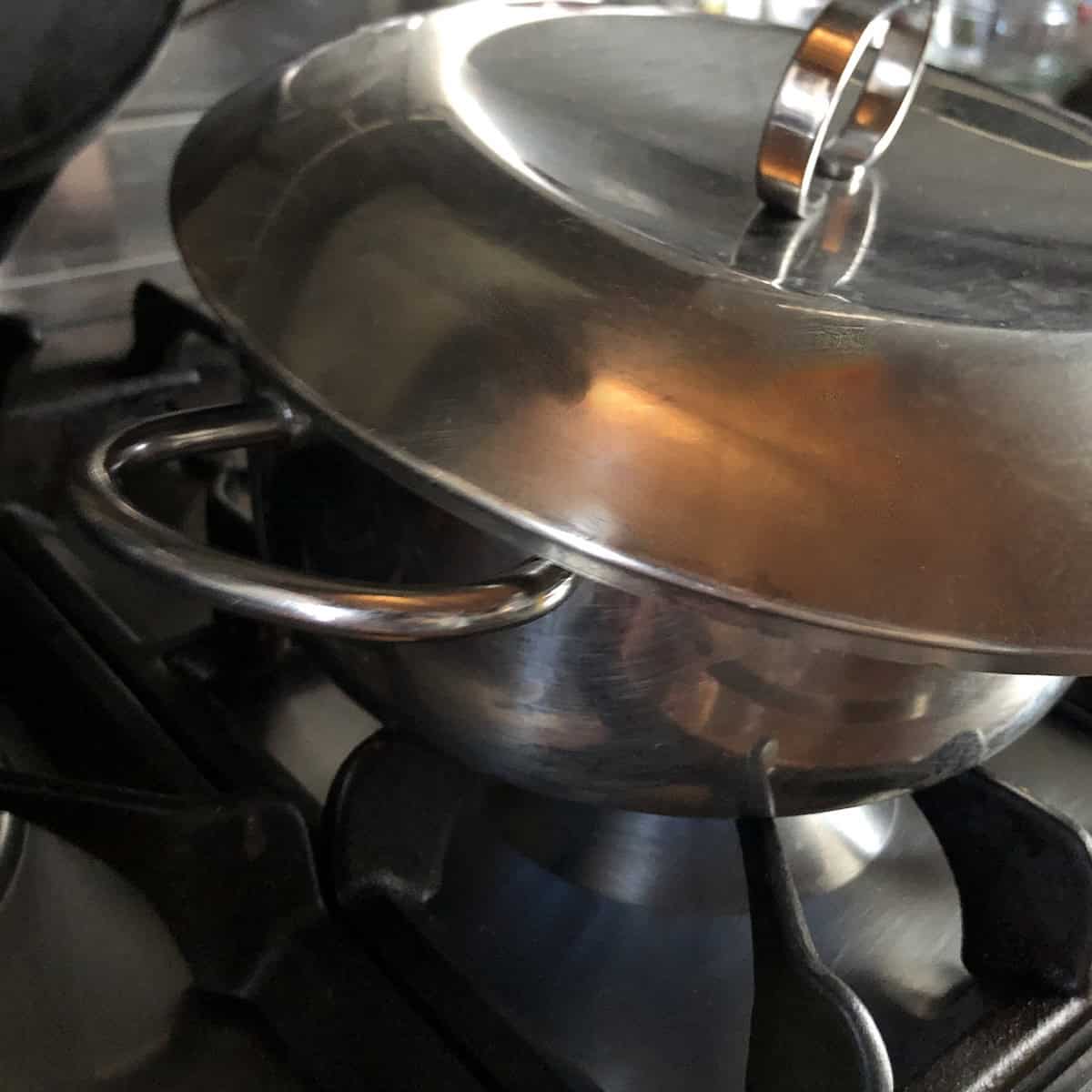 A lid partially covering the simmering pot of chicken tortilla soup broth as it cooks.
