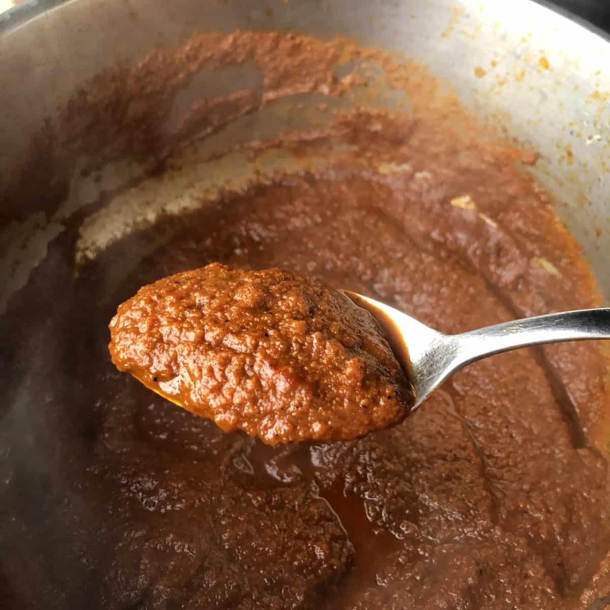 A spoon of the reduced dark red chile tomato paste showing the thick consistency before adding broth for spicy chicken tortilla soup.
