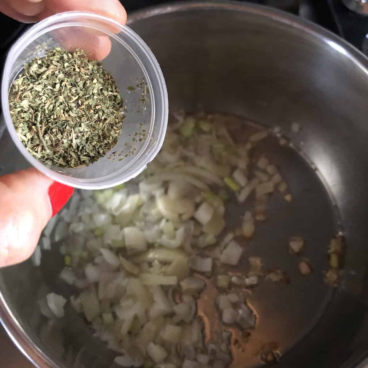 Adding the epazote to the lard, diced onions, and garlic seasoned with salt cooking in a saucepan ready to cook for 4 more minutes until golden brown.
