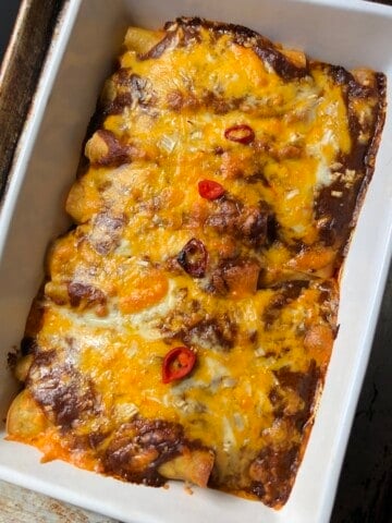 A casserole of baked chicken enchiladas with melted cheese, ancho chile enchilada sauce, and crispy golden tortilla edges.