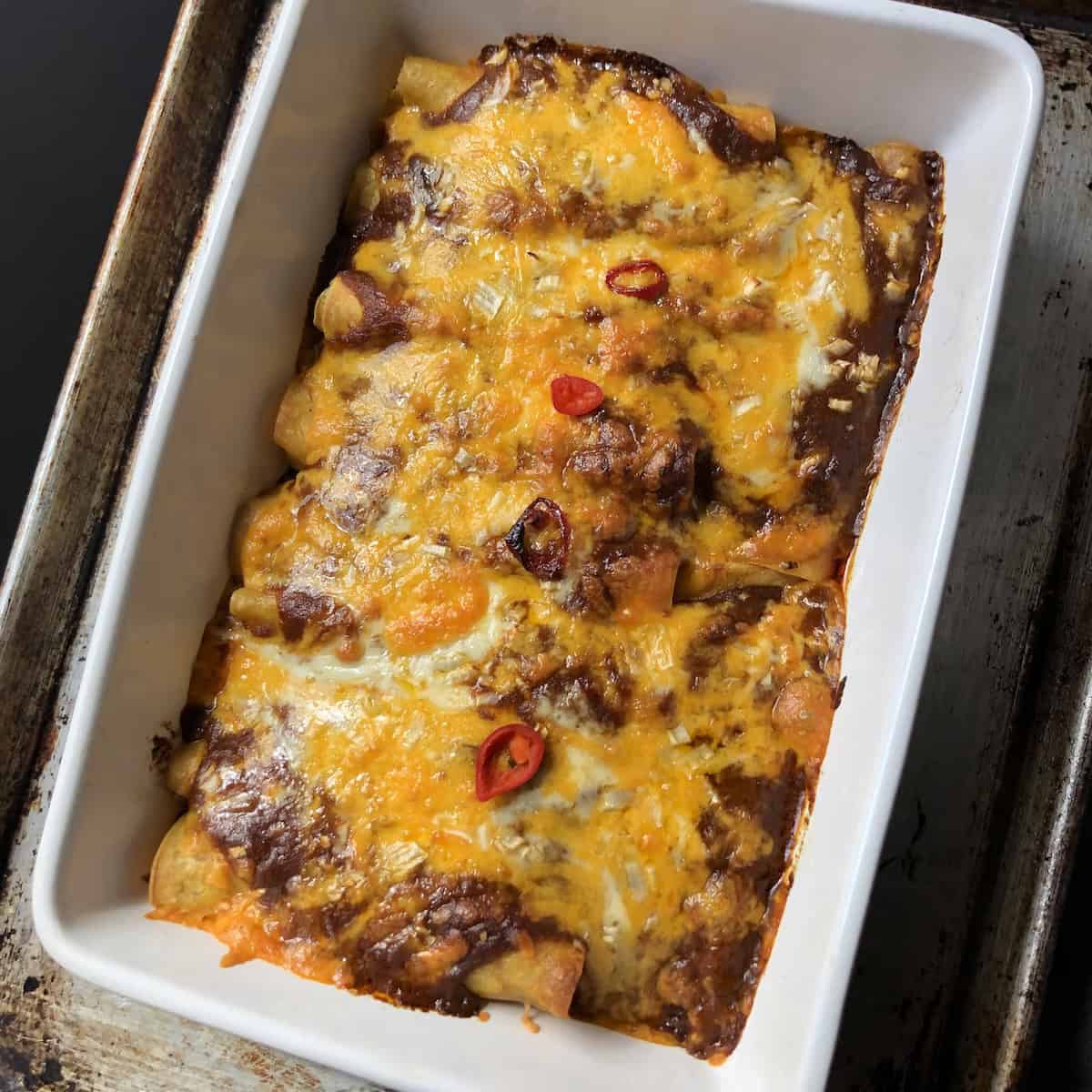 A casserole of baked chicken enchiladas with melted cheese, ancho chile enchilada sauce, and crispy golden tortilla edges.