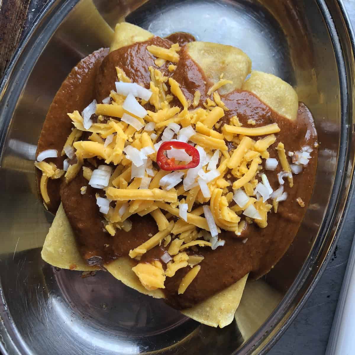 Three assembled chicken enchiladas with ancho chile sauce, cheese, onions, and a red jalapeno slice before baking.