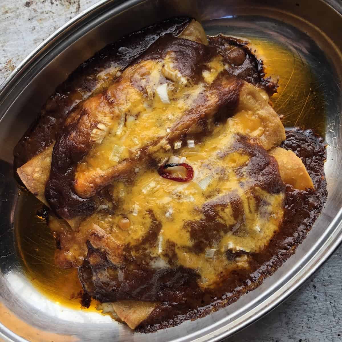 Baked chicken enchiladas with melted cheese, minced onions, and a red chile oil slick in a casserole dish.