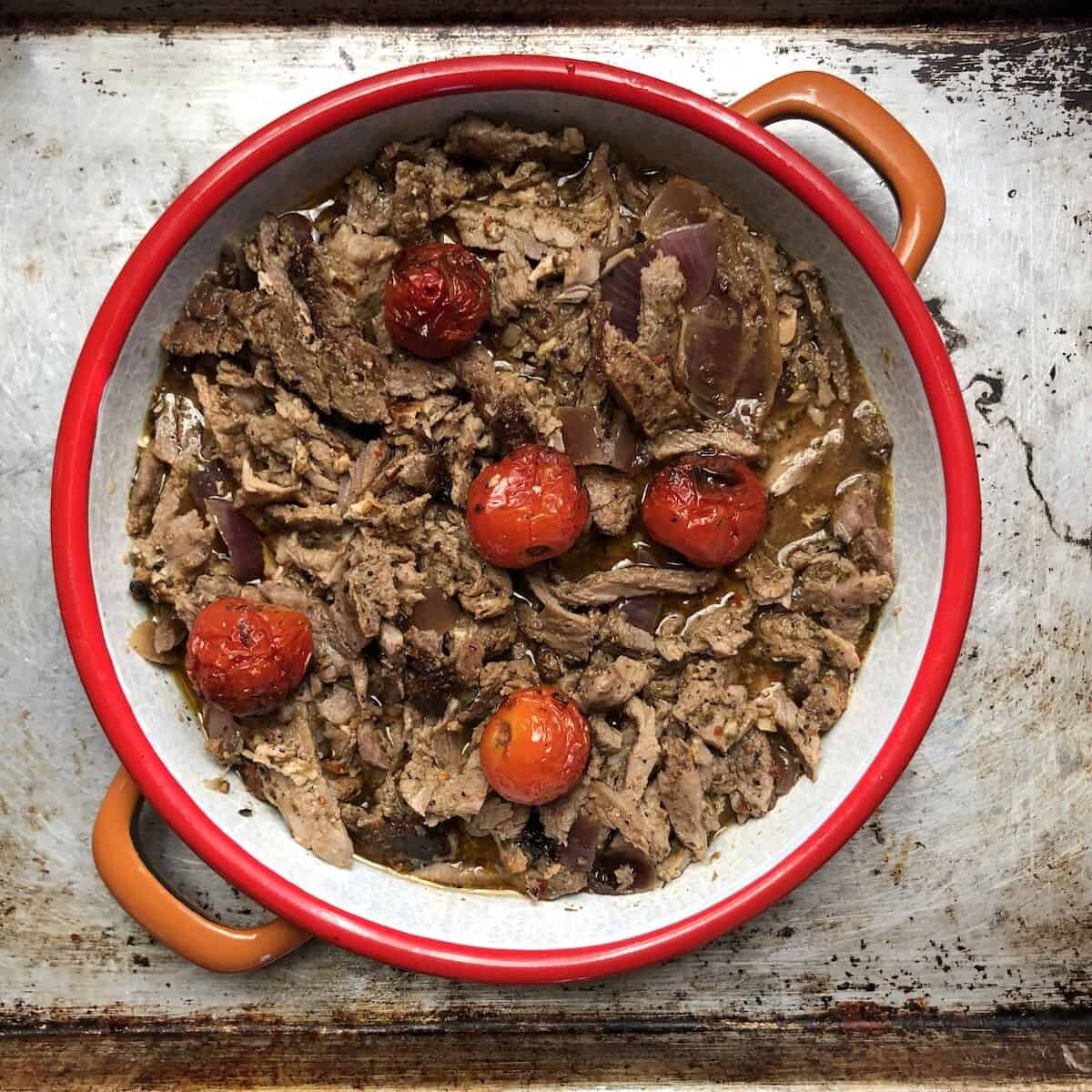 Greek gyro meat shaved from the tower on a serving platter with its baking juices pooled around the tender pork slices.