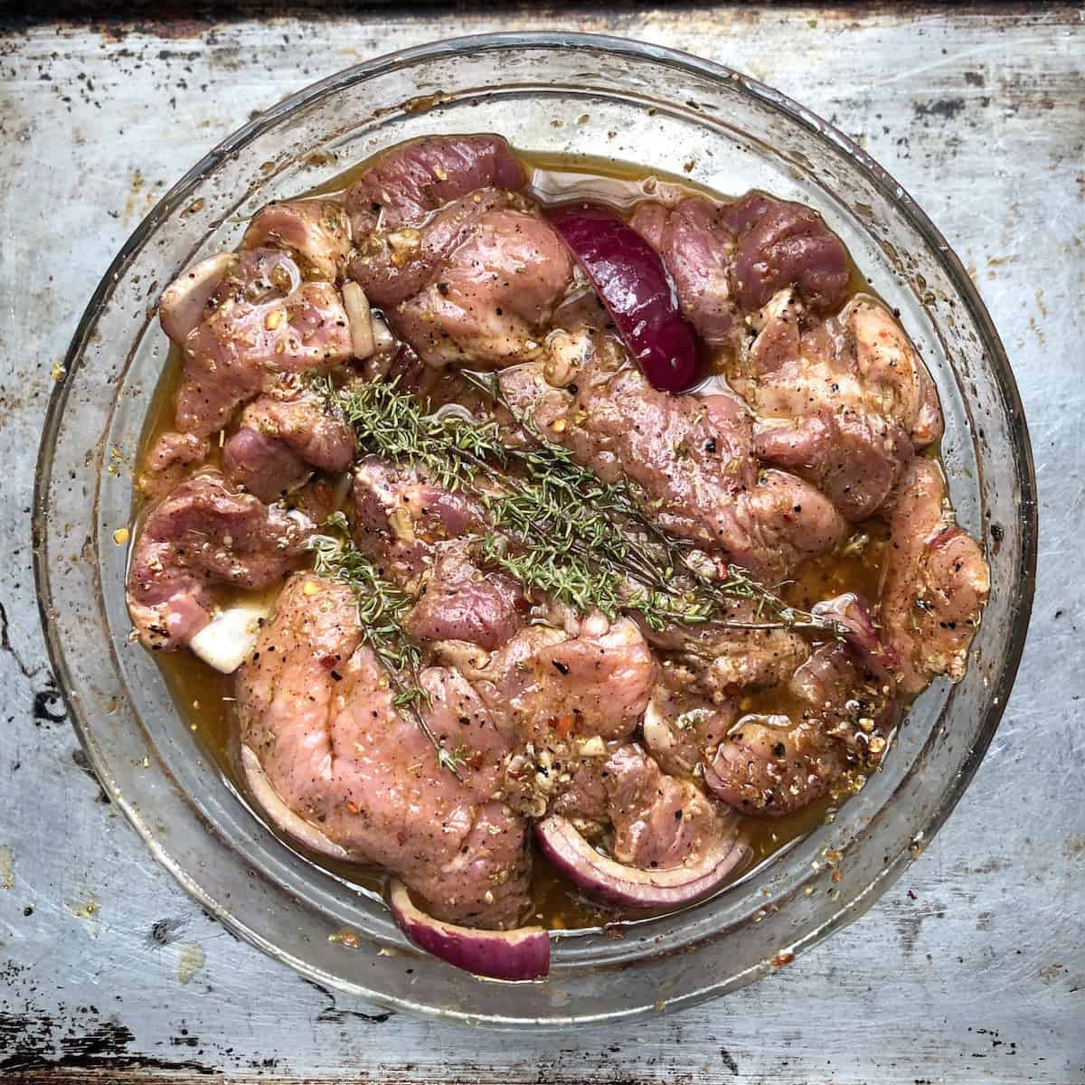 Greek gyros pork slices tossed in homemade gyro seasoning recipe with spices, oil, and vinegar in a bowl ready to marinate overnight.