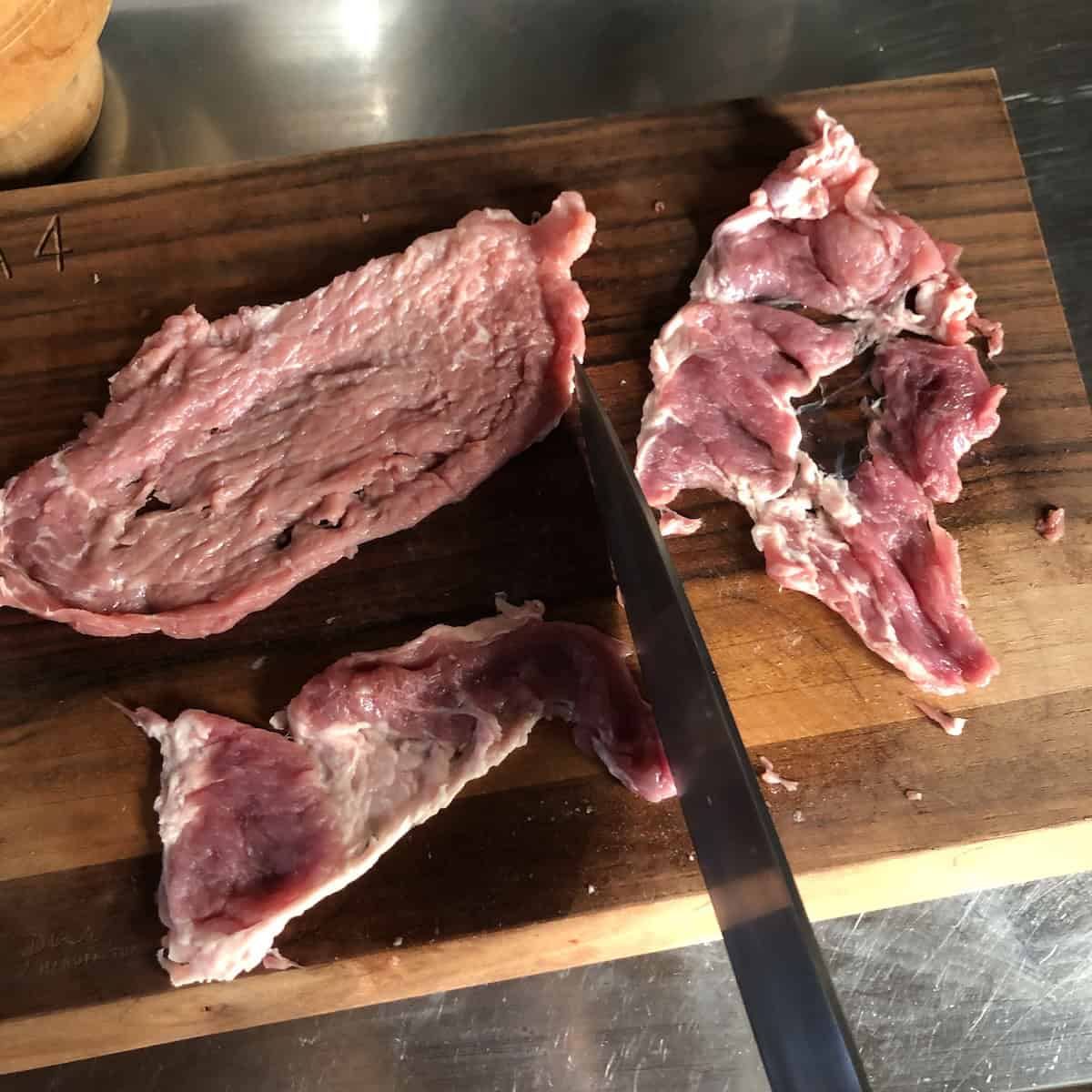Pork slice pounded too thin and torn showing what not to do when preparing pork gyros recipe meat to avoid dry results.