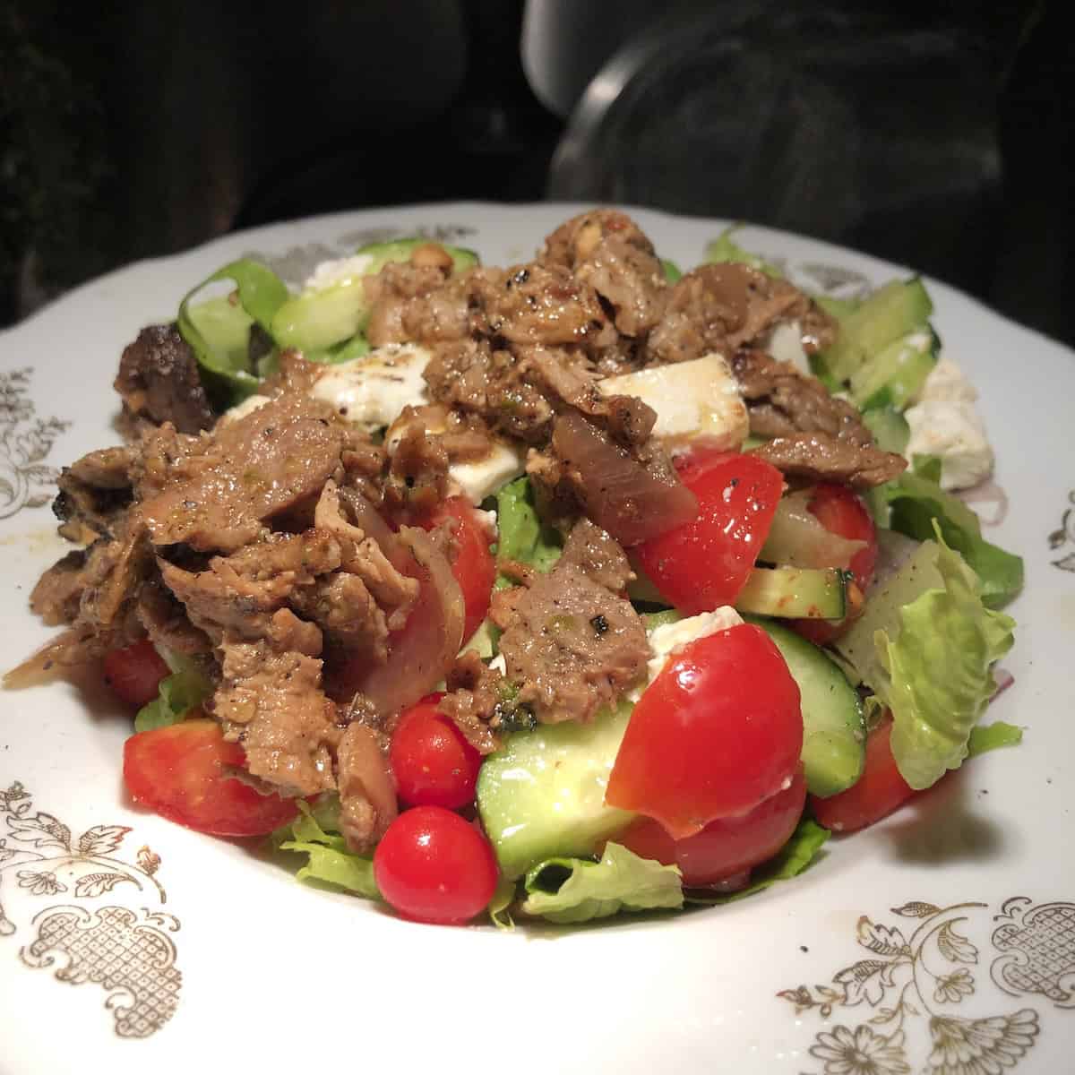 A greek salad with gyro meat on top ready to eat.