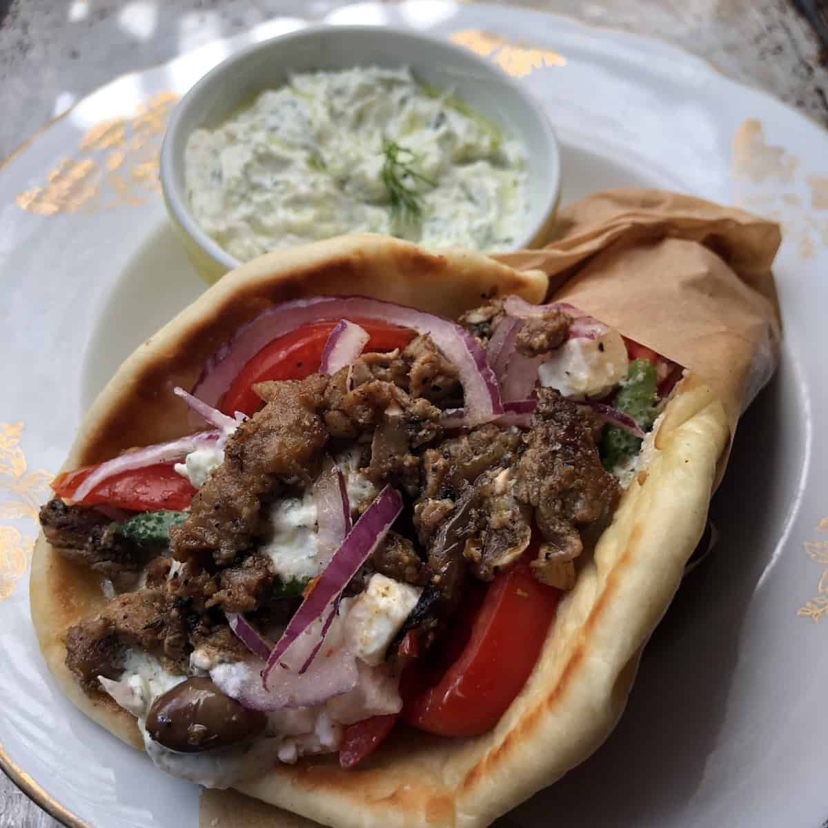 Front facing view of a gyro with a side of tzatziki sauce showing how tender the gyro meat is.
