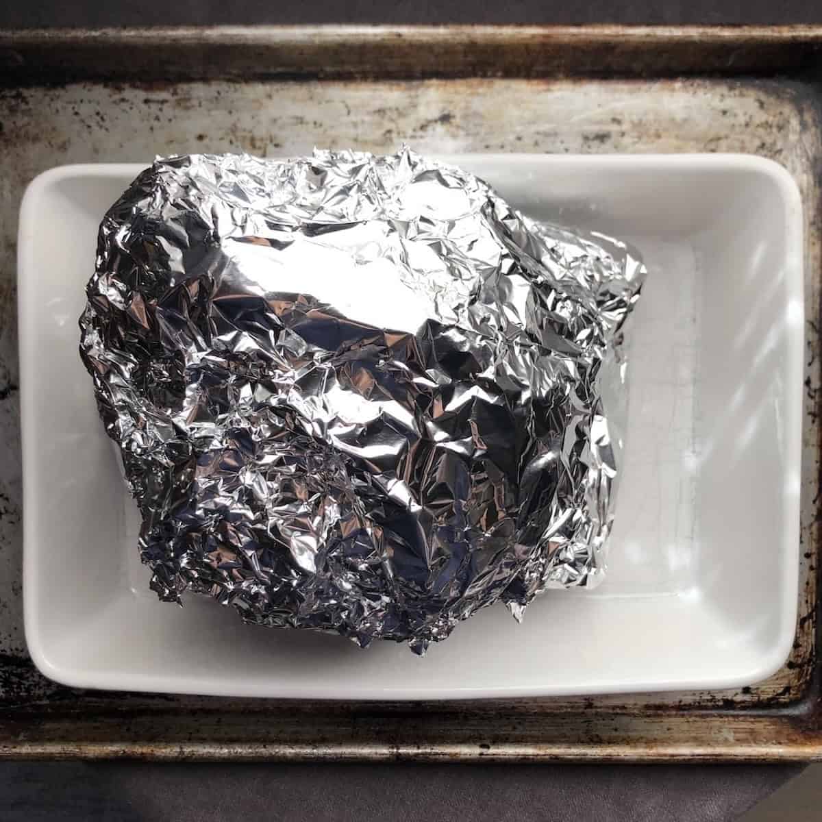 Gyro recipe pork cone encased in aluminum foil as the final layer over parchment, ready to bake low and slow for a tender gyro sandwich.