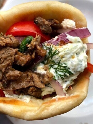 Gyro sandwich closeup of tender pork gyro meat wrapped in a soft Greek pita with tzatziki, feta, tomatoes, cucumbers, and red onions and greek black olives.