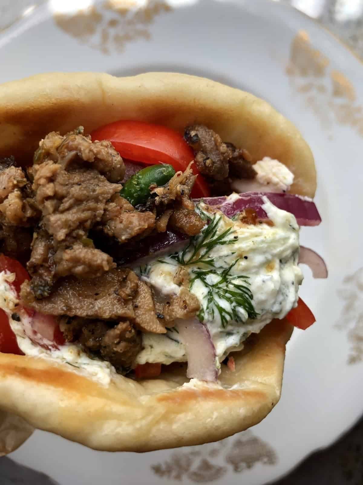 Gyro sandwich recipe closeup of tender pork gyro meat wrapped in a soft Greek pita with tzatziki, feta, tomatoes, cucumbers, and red onions.