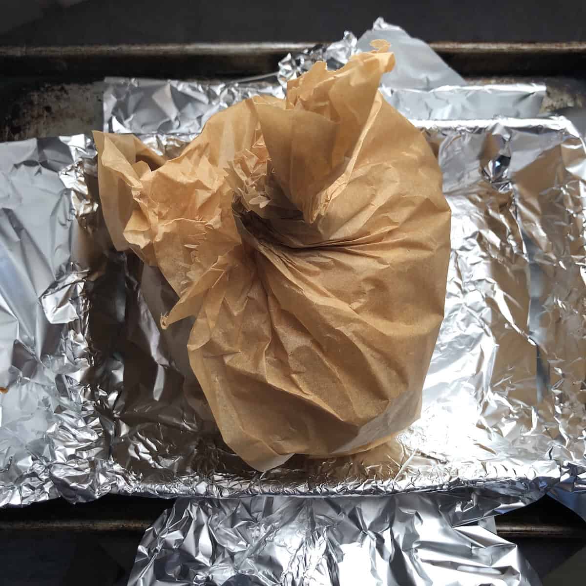 Gyros recipe pork meat cone tightly wrapped in parchment paper and twisted at the top to hold its shape before baking.