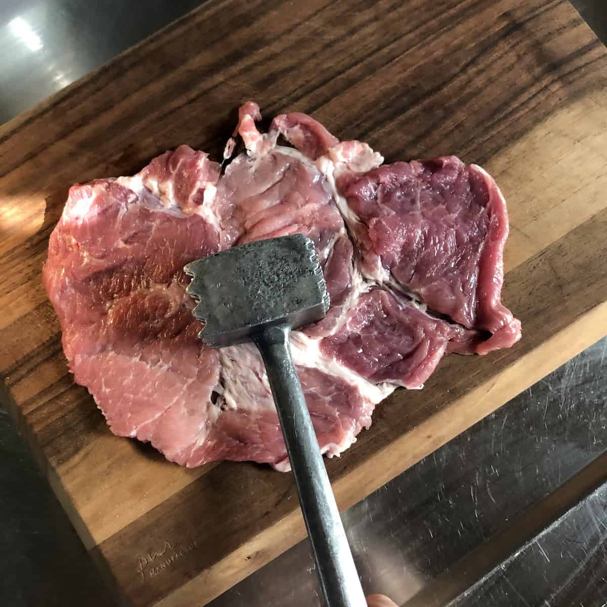Pounding pork slices to an even quarter inch thickness to help tenderize them and help them cook evenly before stacking them on a homemade gyro meat cone.