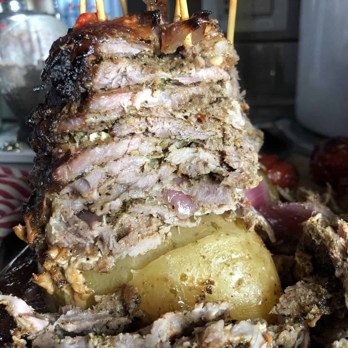 How to make gyros at home showing crispy pork gyro meat being sliced off the tower with half the stack still standing.